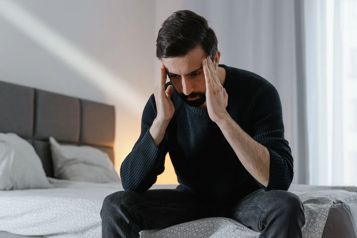 Homme soucieux assis au bord du lit, la tête entre les mains